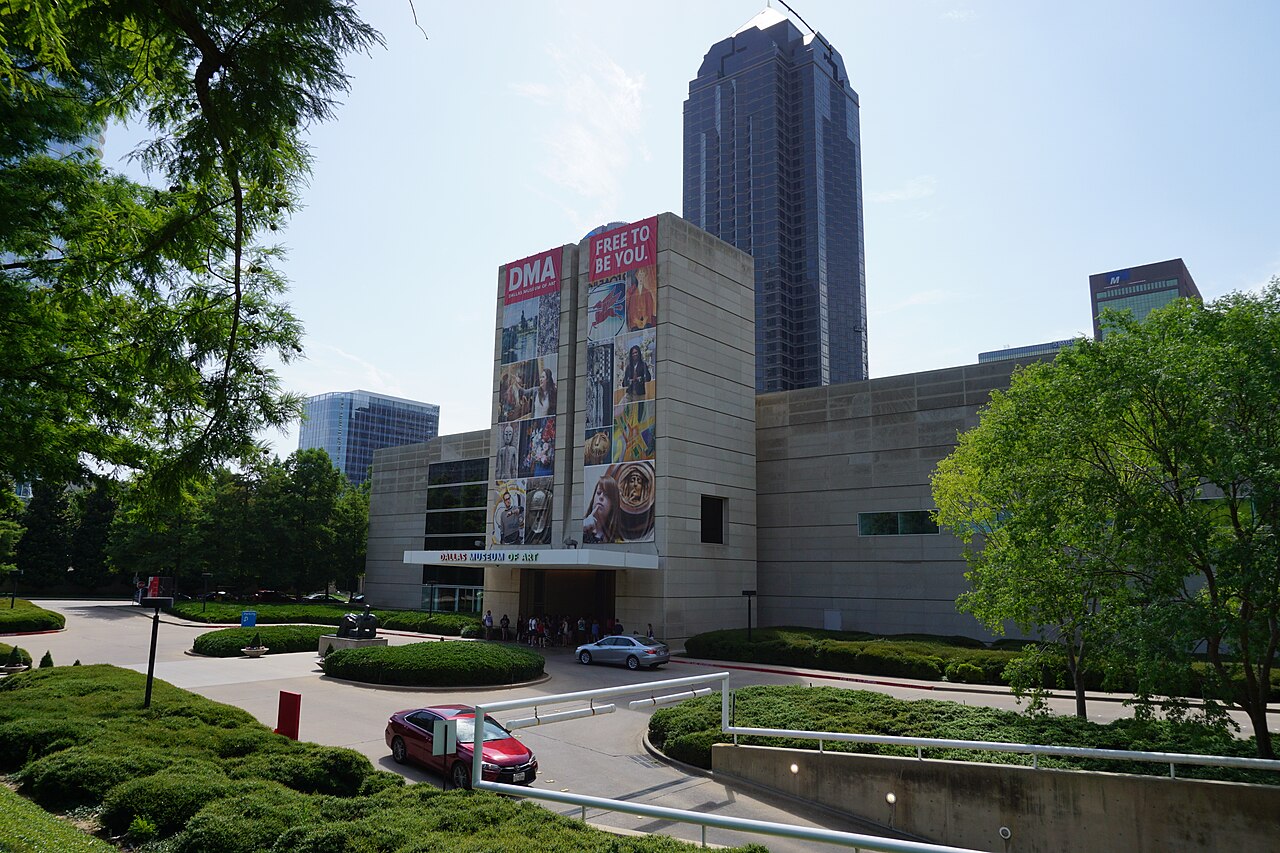 Real exterior of the Dallas Museum of Art framed by green trees and downtown architecture